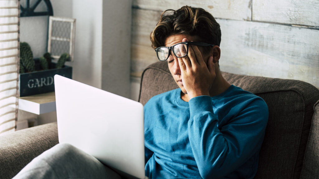 Stressed student at home studying with personal laptop computer - tired teenager for school work -internet. addiction for game or job search concept - indoor technology activity